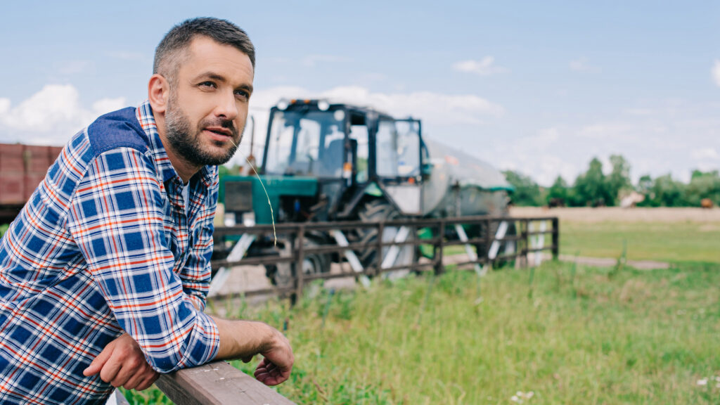 handsome middle aged farmer leaning at fence and looking away at farm